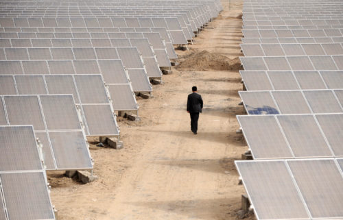 a man walking between rows of solar panels in xinjiang, china